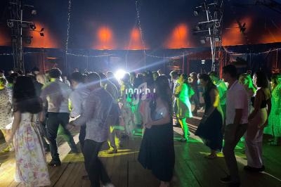 Personnes dansant sous une tente éclairée par des lumières colorées, ambiance festive et conviviale.
