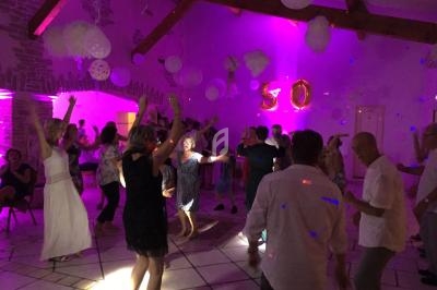 Groupe de personnes dansant dans une salle décorée avec des lumières colorées et des ballons marquant un anniversaire.