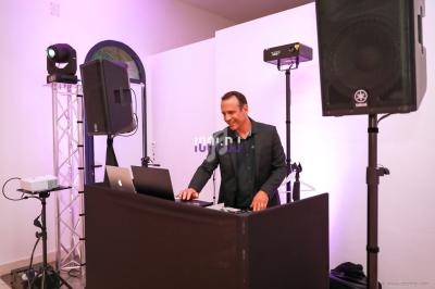 Un DJ mixant de la musique sur une table équipée d'ordinateurs et d'enceintes dans une salle éclairée.