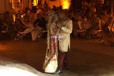 Un couple en tenue traditionnelle danse dans une salle éclairée par des lumières chaudes devant des invités assis.