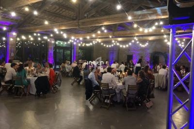 Salle de réception avec des invités assis à des tables rondes, éclairée par des guirlandes lumineuses suspendues.
