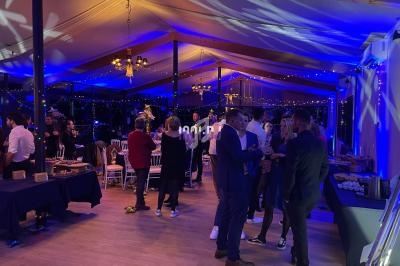 Des personnes discutent dans une salle éclairée de lumières bleues, avec des tables dressées et une ambiance festive.