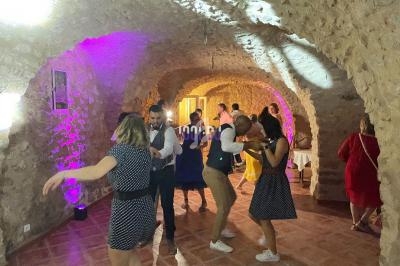 Des personnes dansent dans une salle voûtée en pierre éclairée par des lumières colorées.