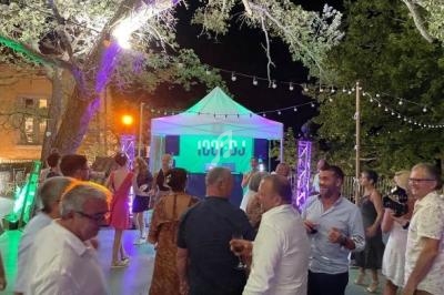 Groupe de personnes discutant et dansant en soirée en plein air, avec un DJ sous une tente éclairée.