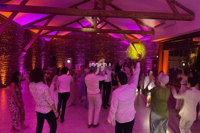 Personnes dansant dans une salle éclairée par des lumières colorées, avec des poutres apparentes au plafond.