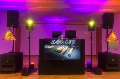 Installation de matériel de karaoké avec écran central, enceintes, lumières colorées et décor lumineux triangulaire.