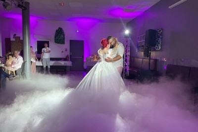 Un couple danse leur première danse de mariage sur une piste entourée de fumée et éclairée par des lumières violettes.