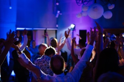 Groupe de personnes levant les bras lors d'une fête dans une salle éclairée par des lumières colorées.