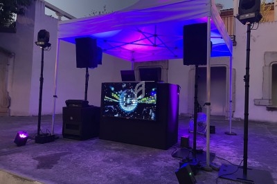 Installation DJ en extérieur sous une tente blanche, éclairée par des lumières colorées et équipée de haut-parleurs.