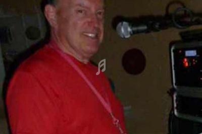 Homme en t-shirt rouge devant un microphone, avec un équipement audio en arrière-plan.