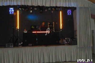 Un DJ mixe sur une scène éclairée par des néons et des projecteurs, entouré de rideaux gris.