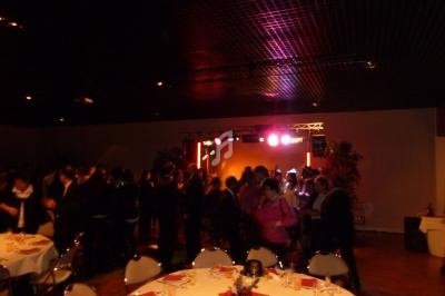 Salle de réception sombre avec des invités dansant près d'une scène éclairée par des lumières colorées.