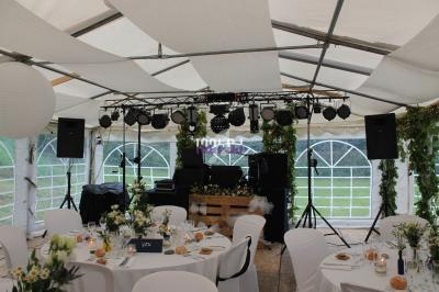 Salle de réception sous une tente avec tables dressées, décorations florales et équipement de sonorisation en arrière-plan.