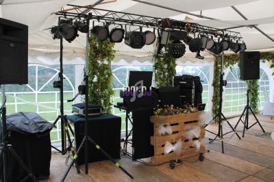 Équipement de sonorisation et éclairage installé sous une tente, avec décoration végétale et caisse en bois.