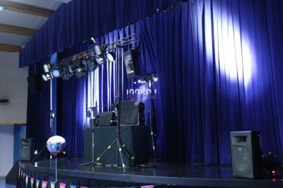 Scène de spectacle avec rideaux bleus, éclairages suspendus, matériel audio et boule disco au premier plan.