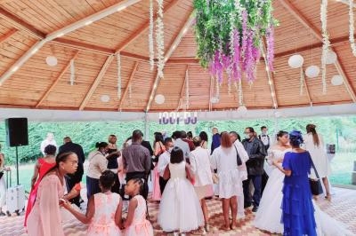 Groupe de personnes rassemblées sous un kiosque en bois décoré de fleurs suspendues lors d'une célébration.