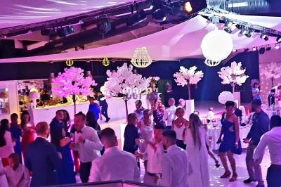 Salle de réception décorée avec des arbres lumineux et des guirlandes, où des invités dansent et discutent.