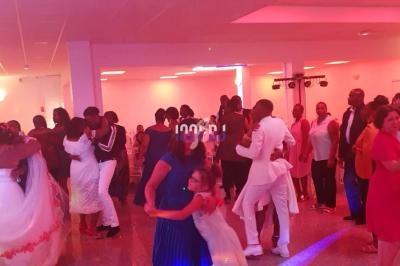 Des couples et des invités dansent dans une salle de réception éclairée par des lumières roses.