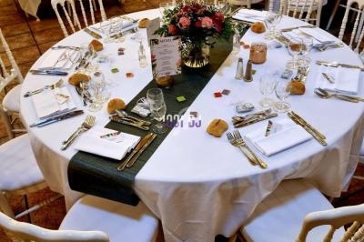 Table ronde dressée pour un repas, avec nappes blanches, chemin de table vert, vaisselle et centre de table fleuri.