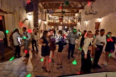 Des personnes dansent dans une salle de réception éclairée par des lumières colorées, avec une ambiance festive.