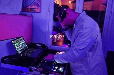 Un DJ mixe de la musique sur une table de mixage, avec un ordinateur portable ouvert, dans une ambiance lumineuse violette.