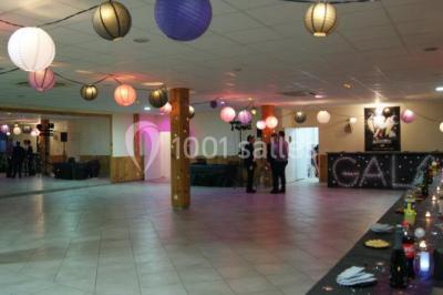 Salle de réception décorée avec des tables alignées, nappes grises, serviettes bleues et chaises rouges.