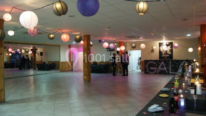 Salle décorée avec des guirlandes lumineuses et des lanternes colorées, tables dressées et quelques personnes présentes.