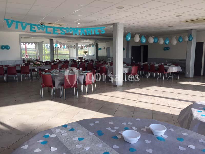 Salle de réception décorée pour un mariage, avec tables dressées, chaises rouges et guirlandes bleues suspendues.