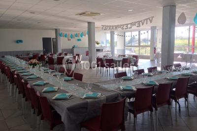Salle de réception décorée avec des tables alignées, nappes grises, serviettes bleues et chaises rouges.