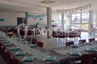 Salle de réception décorée avec des tables alignées, nappes grises, serviettes bleues et chaises rouges.
