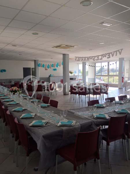 Salle de réception décorée avec des tables alignées, nappes grises, serviettes bleues et chaises rouges.