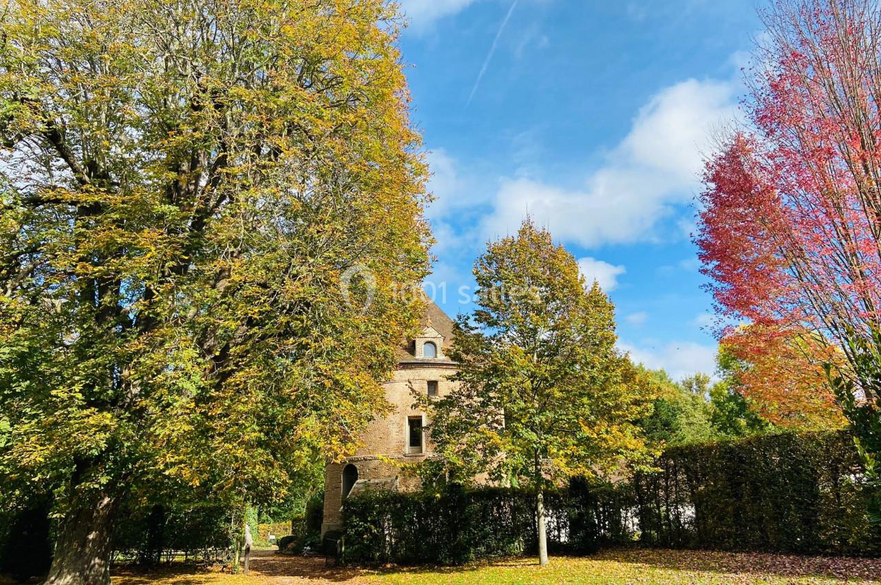 Maison en pierre entourée d'arbres aux feuillages d'automne sous un ciel bleu partiellement nuageux.