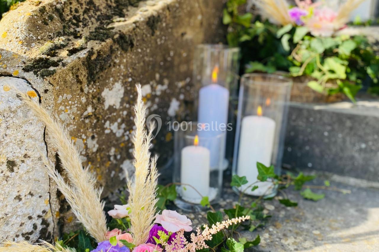 Composition florale avec roses, gerberas et herbes de la pampa, disposée sur des marches en pierre avec des bougies allumées.