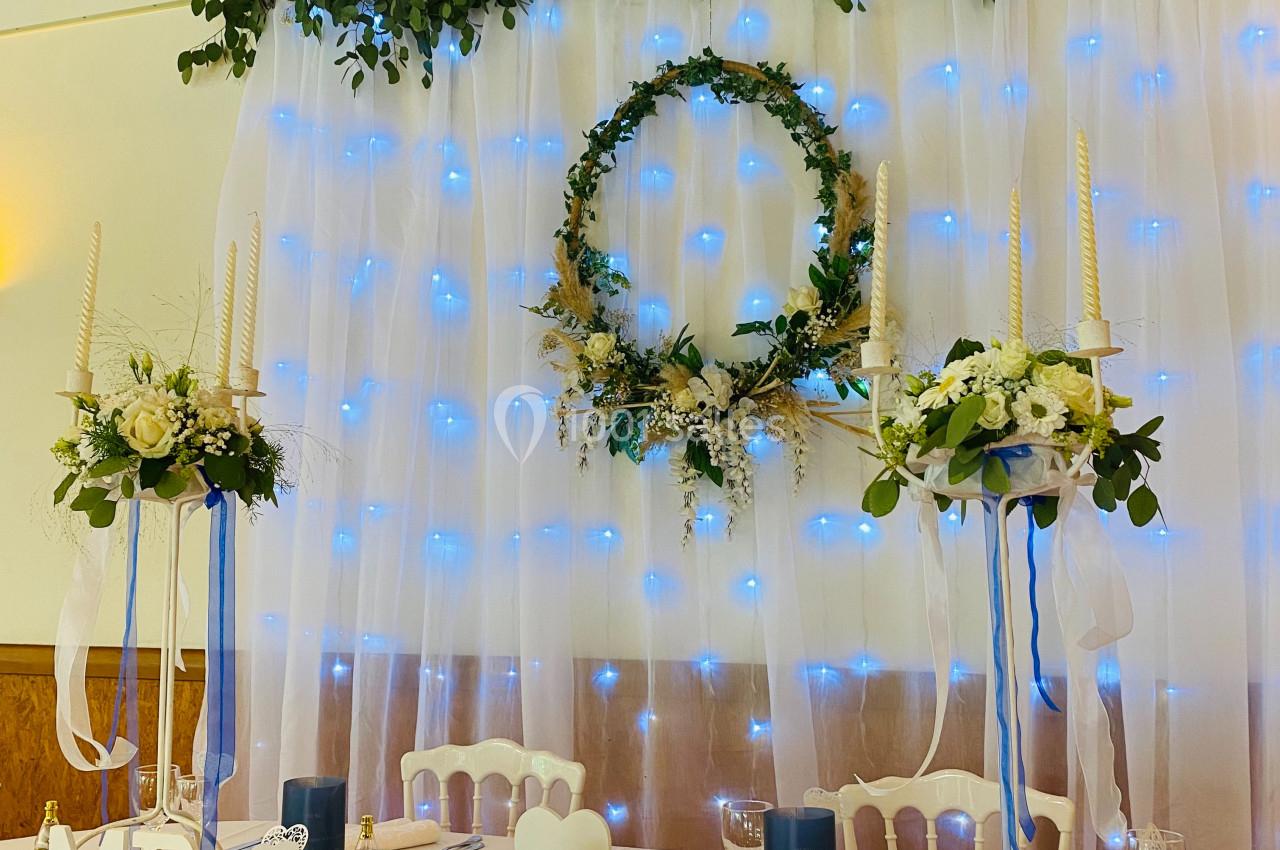Table de mariage décorée avec des fleurs, bougies, et lettres ’MR & MRS’, devant un fond lumineux et végétal.