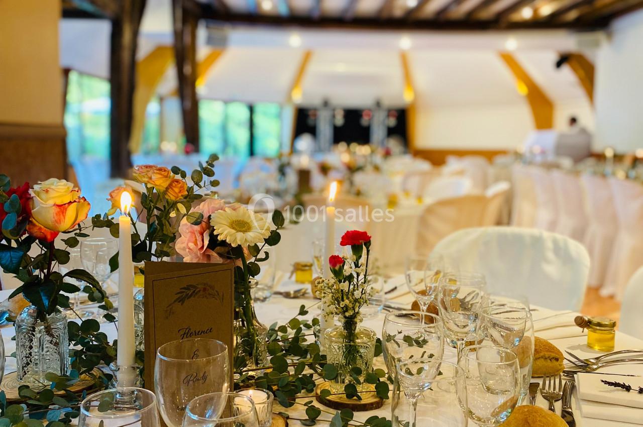 Salle de réception décorée avec des tables dressées, ornées de fleurs, bougies et vaisselle élégante.