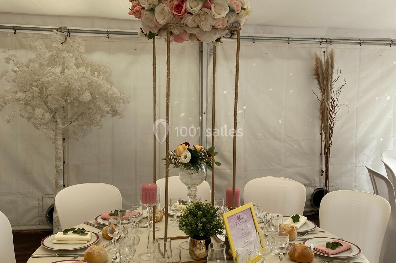 Table de réception élégante avec nappes blanches, vaisselle raffinée, centre de table fleuri et décorations pastel.