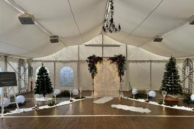 Décoration festive sous une tente avec arche lumineuse, sapins de Noël, guirlandes et sol en bois.