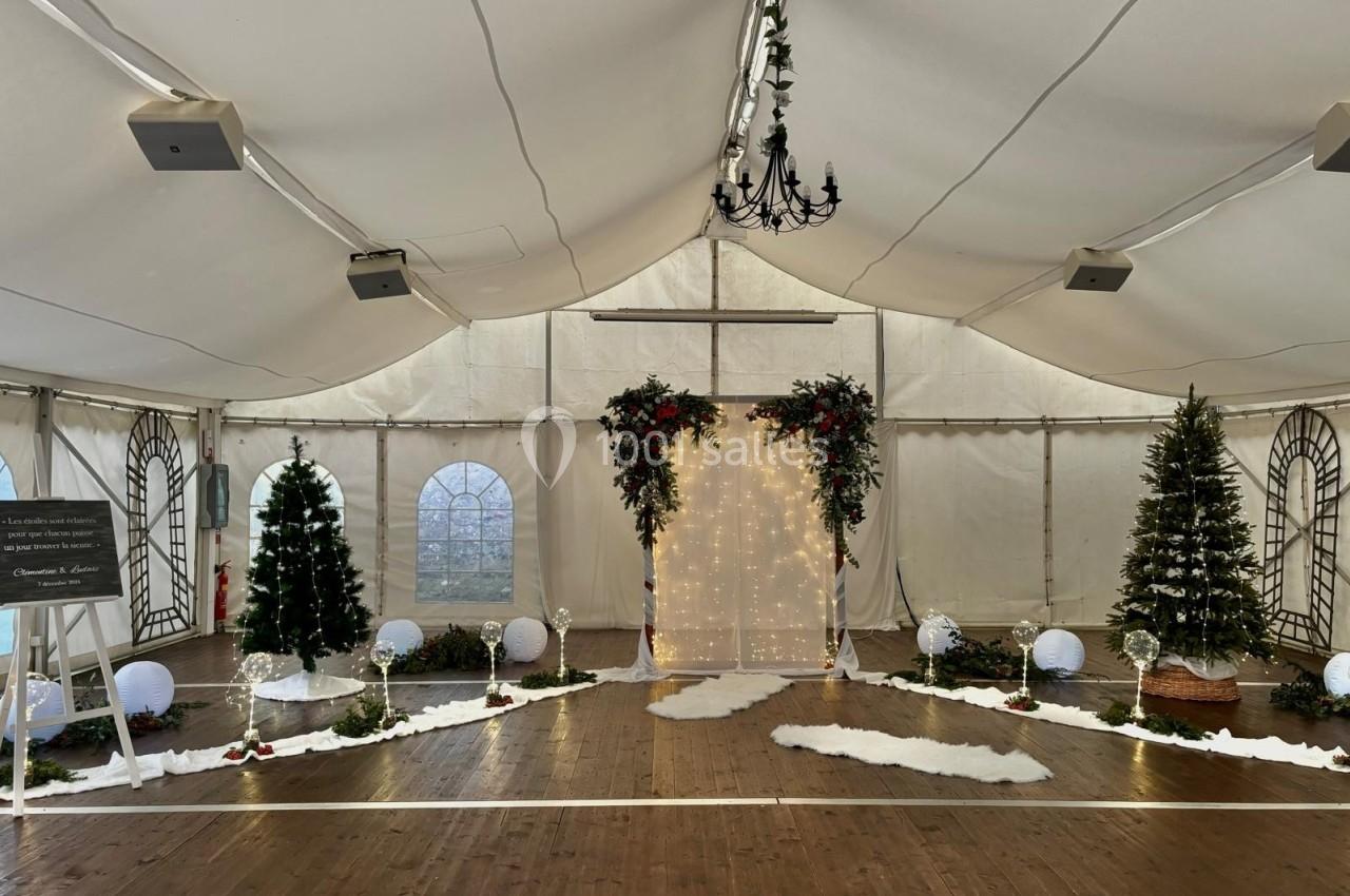 Décoration festive sous une tente avec arche lumineuse, sapins de Noël, guirlandes et sol en bois.