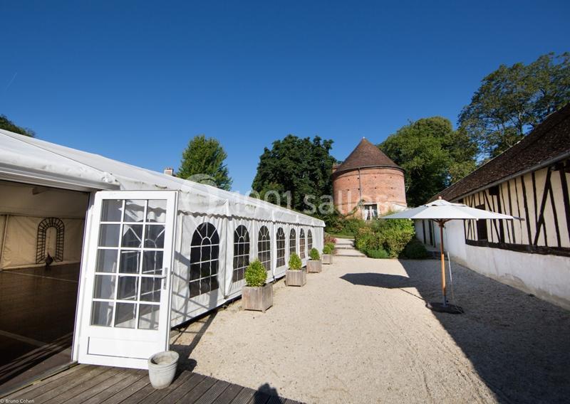 Cour extérieure avec une tente blanche, un pigeonnier en briques, des arbres et des bâtiments à colombages.