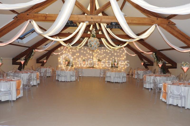 Salle de réception décorée avec des guirlandes lumineuses, des tables dressées et des drapés suspendus au plafond.