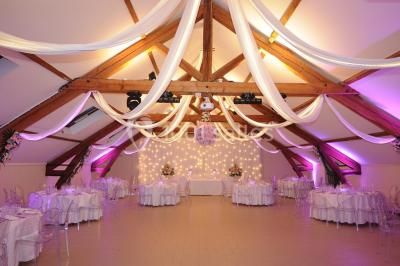 Chambre mansardée avec un lit double blanc, parquet au sol, mur beige et lumière naturelle provenant d'une porte-fenêtre.