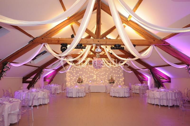 Salle de réception décorée avec des voilages blancs suspendus, éclairage rose et tables dressées pour un événement.