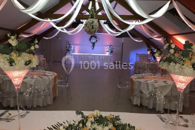 Chambre mansardée avec un lit double blanc, parquet au sol, mur beige et lumière naturelle provenant d'une porte-fenêtre.