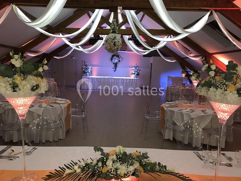 Salle de réception décorée avec des tables dressées, des fleurs et des guirlandes lumineuses suspendues au plafond.
