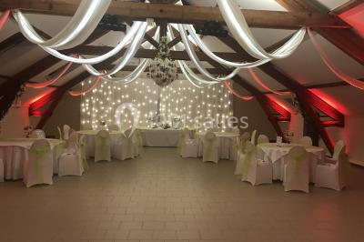 Chambre mansardée avec un lit double blanc, parquet au sol, mur beige et lumière naturelle provenant d'une porte-fenêtre.