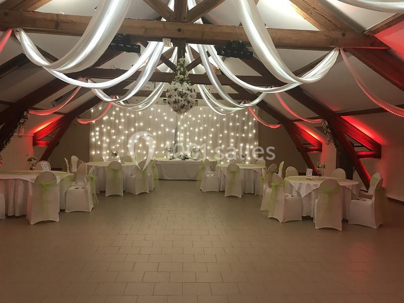 Salle de réception décorée avec des tables rondes, des chaises blanches ornées de nœuds verts et des drapés suspendus.