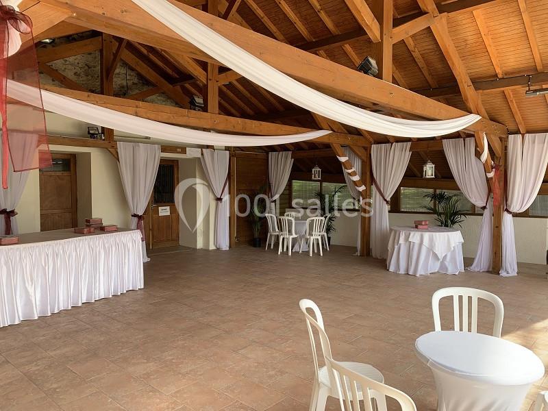 Salle décorée avec des voilages blancs et bordeaux, tables et chaises blanches, ambiance lumineuse et chaleureuse.