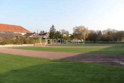 Chambre mansardée avec un lit double blanc, parquet au sol, mur beige et lumière naturelle provenant d'une porte-fenêtre.