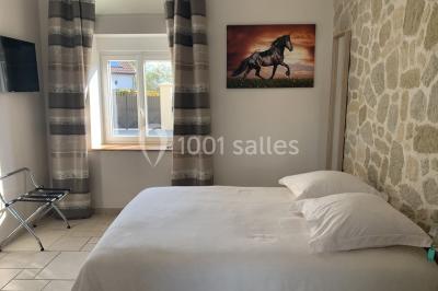 Chambre mansardée avec un lit double blanc, parquet au sol, mur beige et lumière naturelle provenant d'une porte-fenêtre.