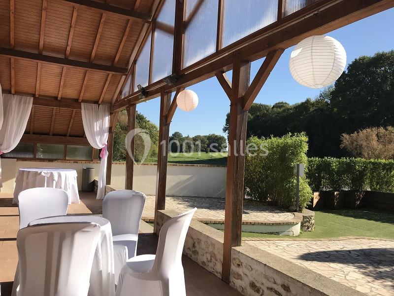 Salle extérieure couverte avec chaises blanches, lanternes suspendues et vue sur un jardin verdoyant.
